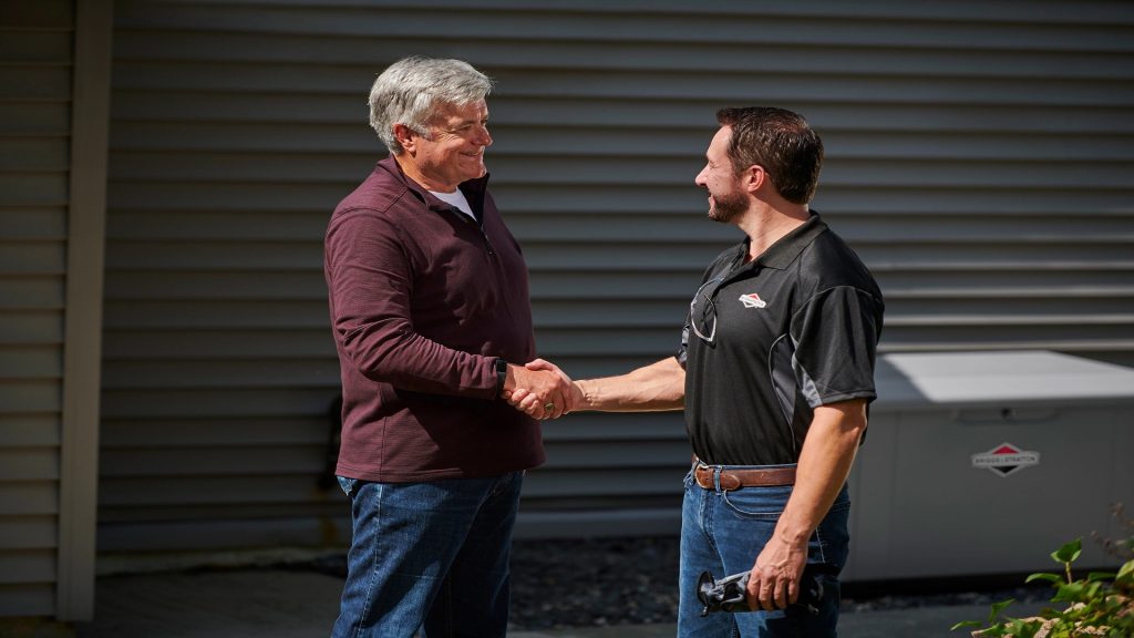 Two men shaking hands in front of a PowerProtect™ DX 26kW Standby Generator.