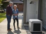 A man and woman standing in front of a PowerProtect™ DX 20kW Standby Generator.